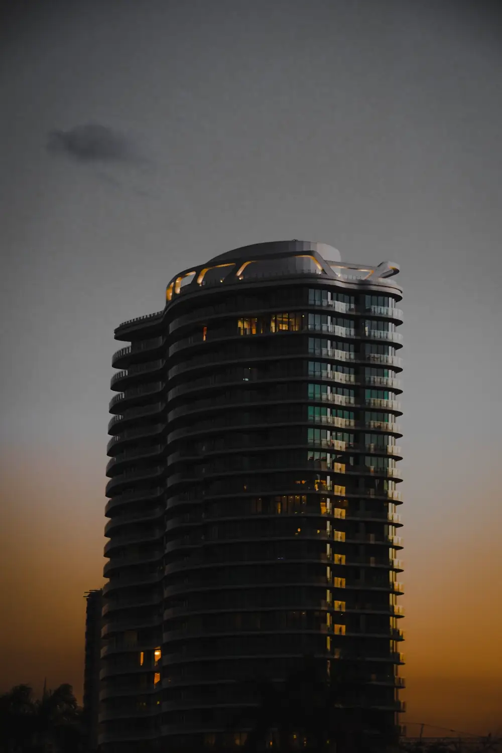 A curved residential tower at dusk with lit windows