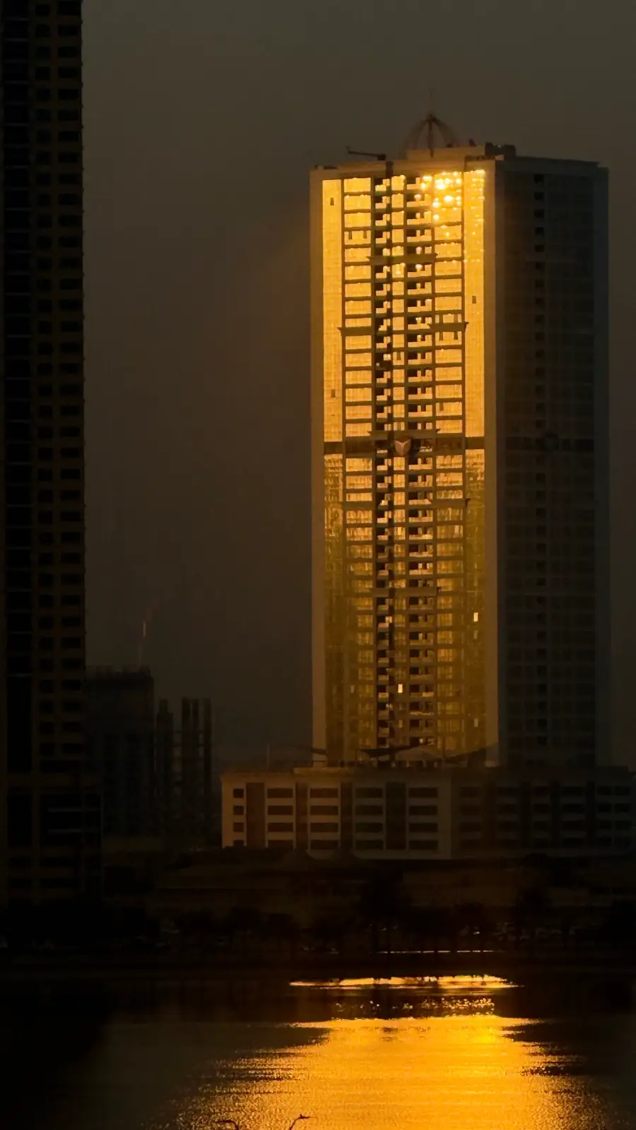 A golden glass residential tower reflected in water at sunset